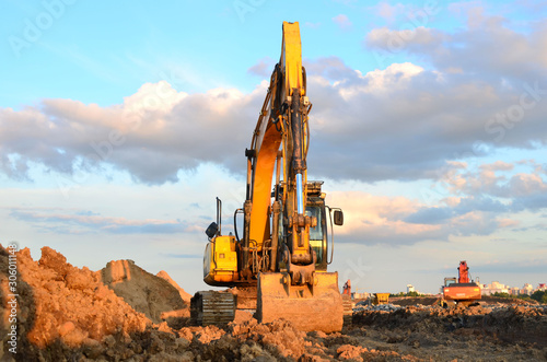 Large tracked excavator digs the ground for the foundation and construction of a new building in the city. Road repair, asphalt replacement, laying or replacement of underground sewer pipes - Image