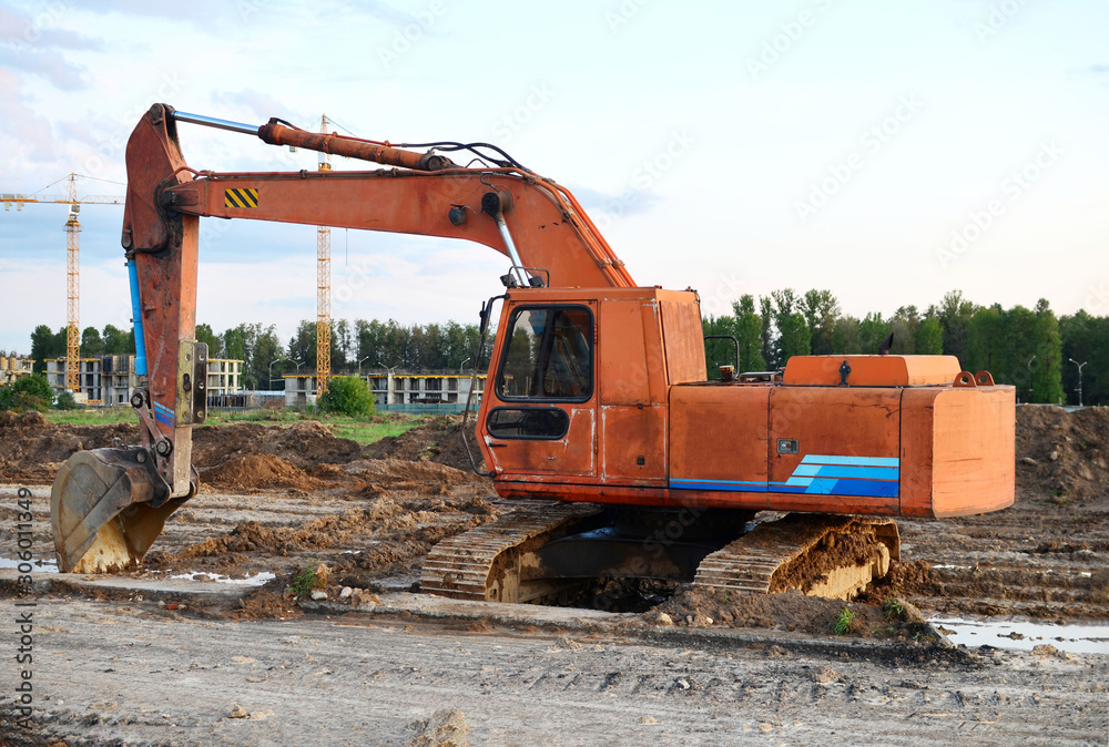 Large tracked excavator digs the ground for the foundation and construction of a new building in the city. Road repair, asphalt replacement, laying or replacement of underground sewer pipes - Image Large tracked excavator digs the ground for the foundation and construction of a new building in the city. Road repair, asphalt replacement, laying or replacement of underground sewer pipes - Image