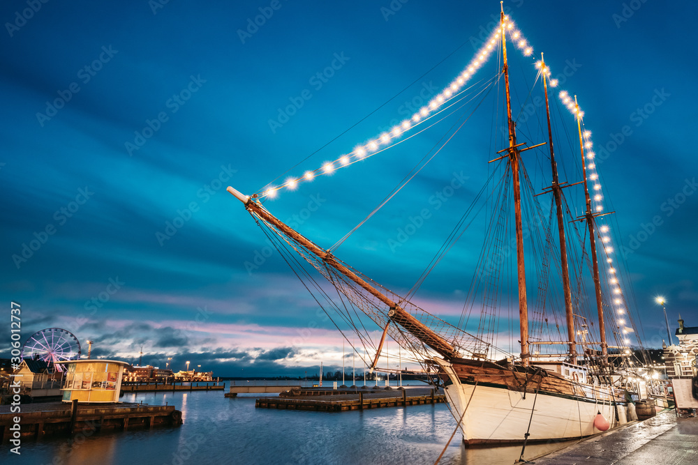 Helsinki, Finland. Old Wooden Sailing Vessel Ship Schooner Is Moored To The City Pier, Jetty. Unusual Cafe Restaurant In City Center In Lighting At Evening Or Night Illumination.