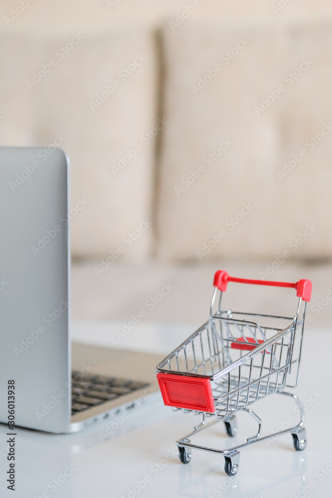 A gray laptop on a table next to a shopping cart from a supermarket. Close up. Vertical.