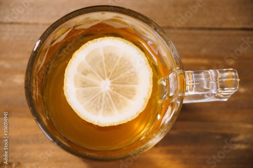 engraved crystal glass with handle with green tea with a slice of lemon inside of the beverage standing on a wooden base view from above