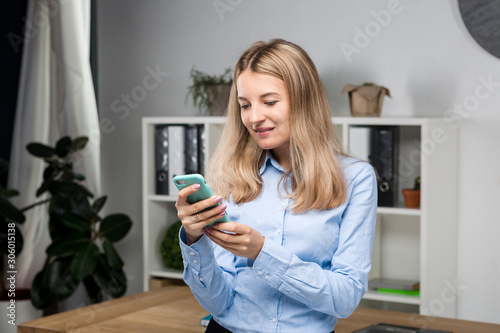 Portrait of businesswoman with mobile phone standing at office. young Caucasian businesswoman holding mobile phone in office. businesswoman using phone. Businesswoman sending message with smartphone