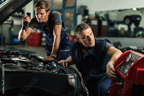 Auto mechanics cooperating while repairing car's air conditioning system in a garage.