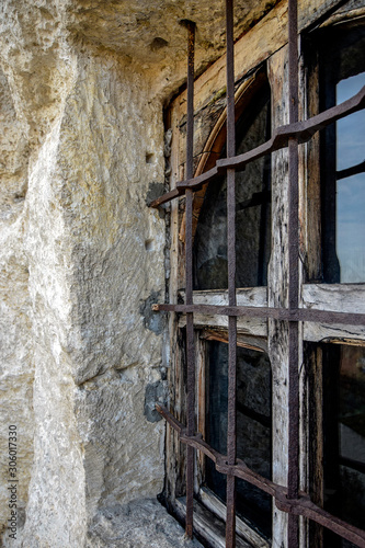 Wooden window of an ancient rock monastery. Protected by forged metal bars. Rusty iron. Close-up.