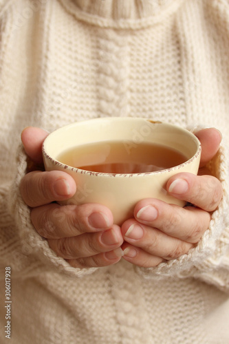 cup of hot fragrant tea in the hands of a woman, texture of a knitted sweater, close-up, copy space, concept of winter or autumn mood, photography for story, social media