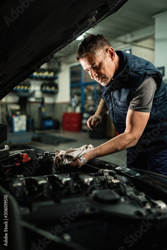 Auto repairman examining oil level of car engine in repair shop.