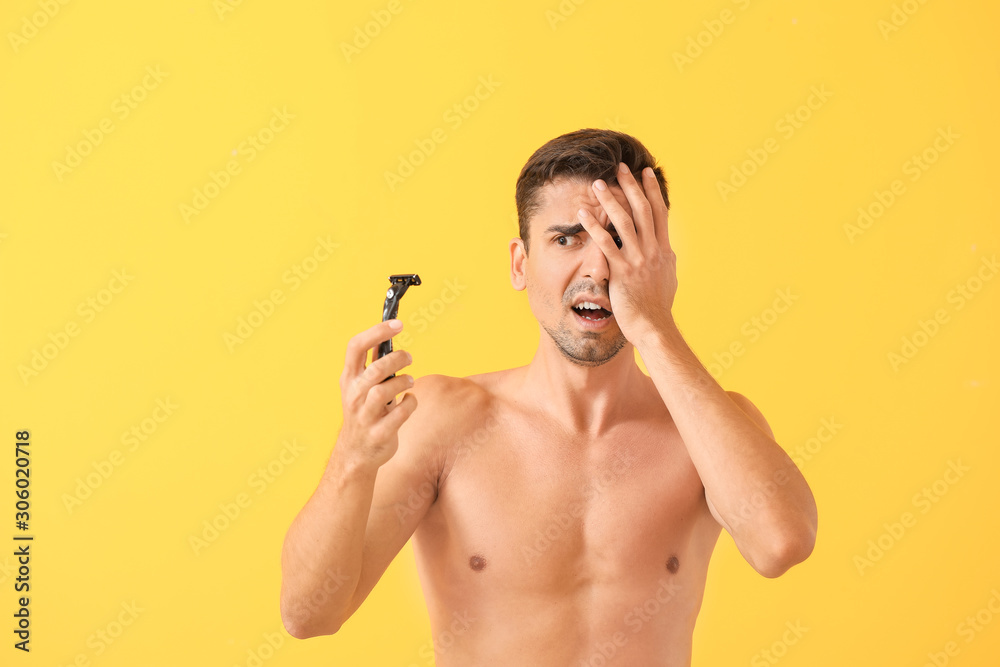 Fototapeta premium Displeased young man with razor on color background