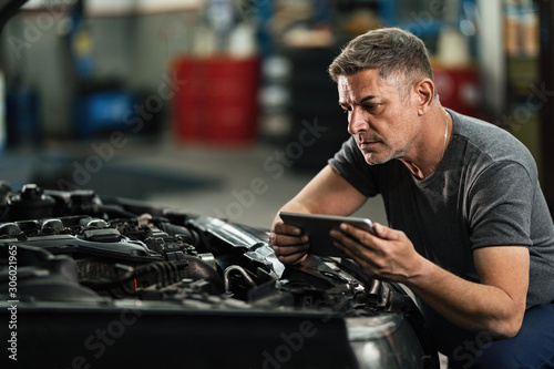 Auto mechanic using touchpad while examining car engine in a workshop.