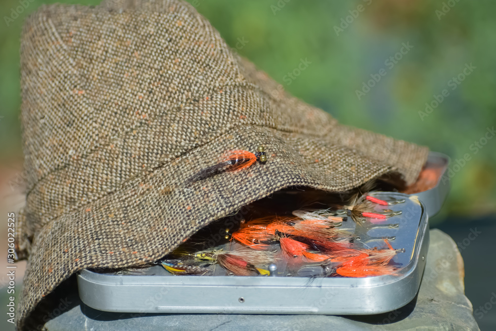 Flyfishing fly box with tied steelhead flies partly covered by an old  fashioned tweed fishing hat. foto de Stock | Adobe Stock