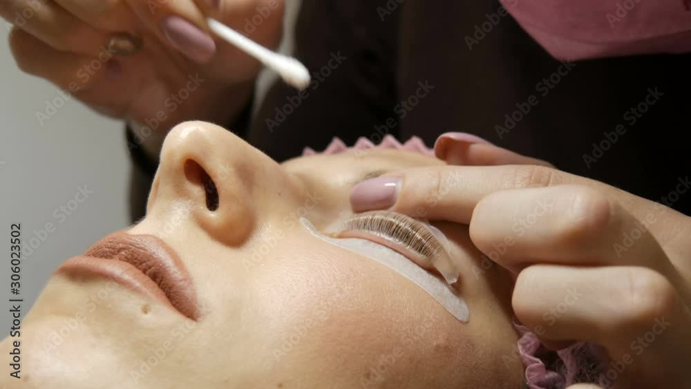 Professional beautician cleans eyelashes from the paint that colored eyelashes to a young beautiful woman Professional beautician cleans eyelashes from the paint that colored eyelashes to a young beautiful woman