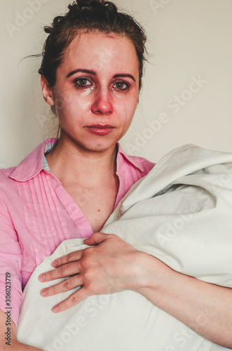 Young mother holds her newborn baby and cries because of post natal depression