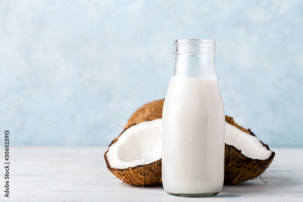 Health content, coconut milk in a glass bottle, coconut halves, light wooden table, close-up