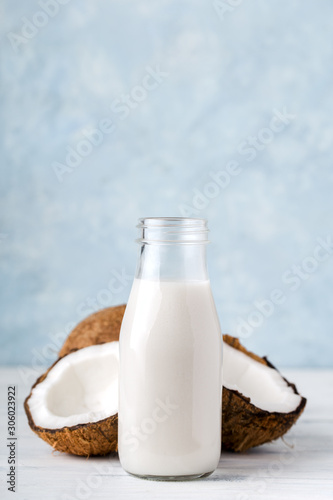 Health content, coconut milk in a glass bottle, coconut halves, light wooden table, close-up, vertical