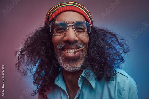 Happy African Rastafarian male smoking cigarettes. Isolated on a blue background.