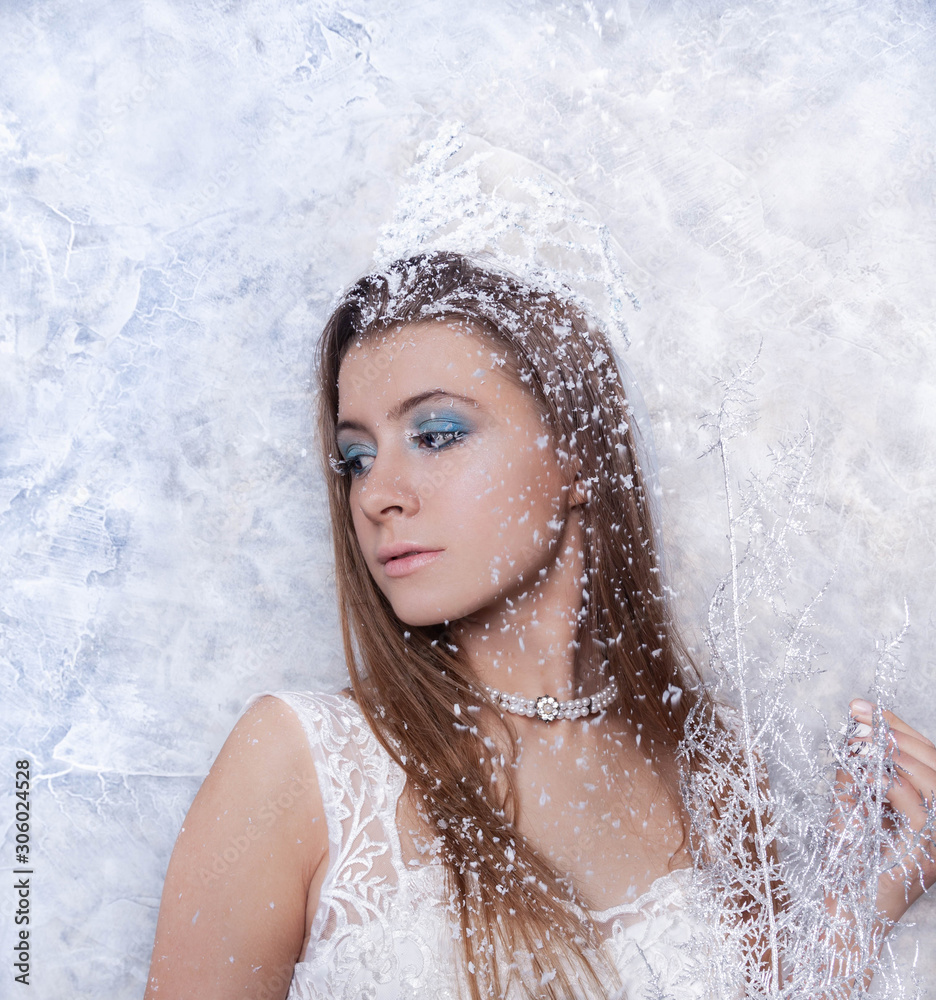 portrait of a beautiful girl looking to the left with a crown on her head and falling snow near her, light background, winter concept