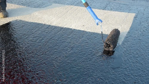 Waterproofing coating. Worker applies bitumen mastic on the foundation. Roofer cover the rooftop polymer modified bitumen waterproofing primer, with a roller brush.