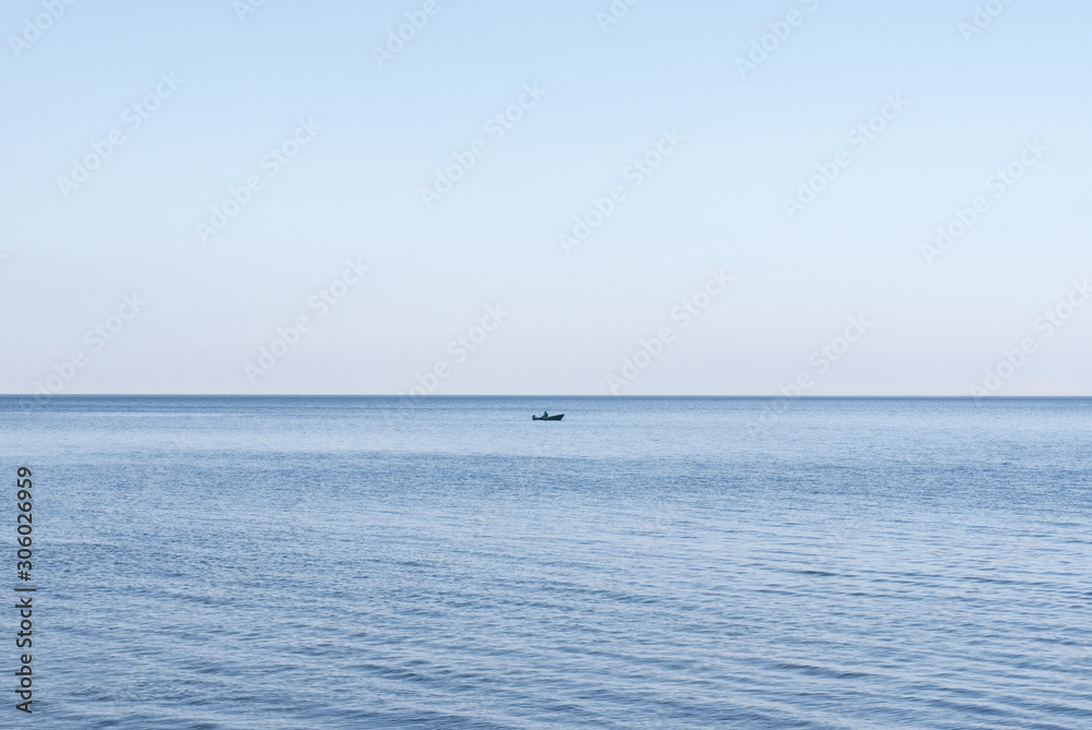 Lone fisherman in a boat with a motor on the water in the middle of a lake or sea