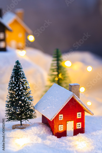 Miniature red wooden house on the snow over blurred Christmas decoration background  toned  daylight