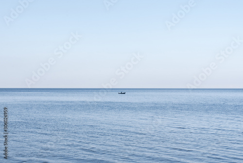 Lone fisherman in a boat with a motor on the water in the middle of a lake or sea