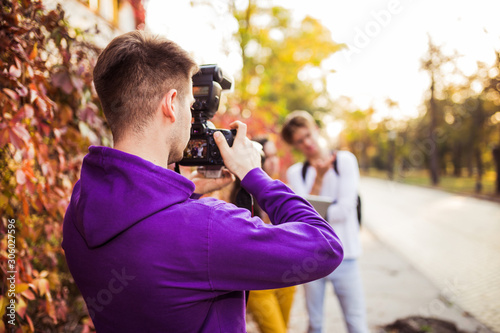 Man photographing his friends or young couple with professional camera on the street.