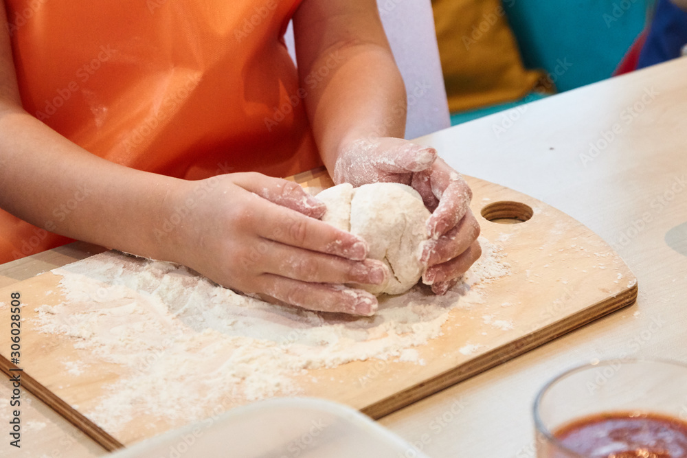 The kid 's learning to make pizza from the dough.