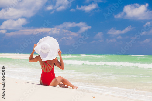 Young woman in bikini and white straw hat relaxing at white caribbean beach