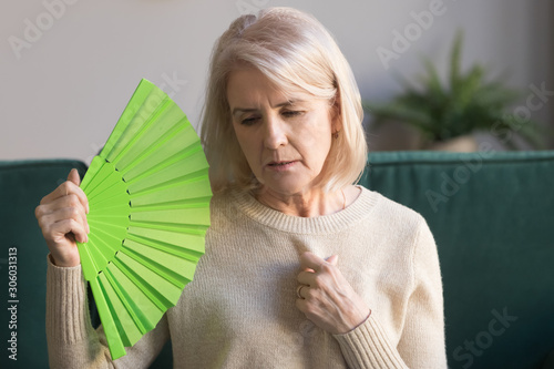 Overheated elderly woman sitting on couch waving green fan