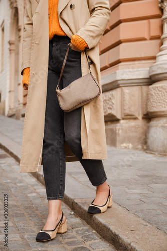 fashion blogger outfit details. fashionable woman wearing beige trench coat, black jeans, slingback ankle shoes and trendy handbag. detail of a perfect fall fashion outfit.