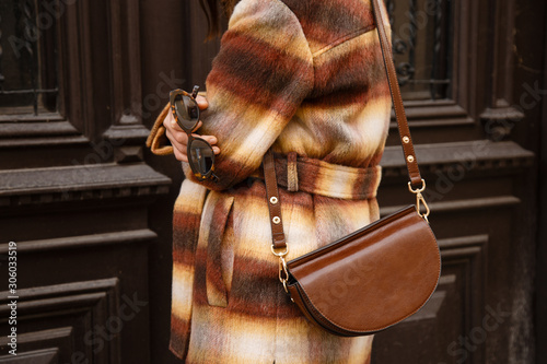 authentic street style portrait of an attractive woman wearing plaid check jacket coat, sunglasses and brown leather bag, crossing the street. fashion outfit details perfect for autumn fall winter