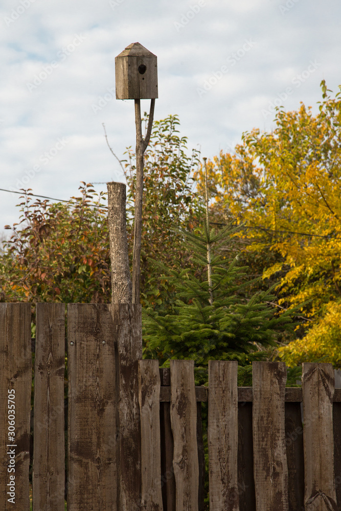 Birdhouse on a tree branch. Simple birdhouse design. Shelter for birds. Birdhouse in backyard behind the wooden fence. Concern for the environment. Autumn landscape. Birdhouse on a tree branch. Simple birdhouse design. Shelter for birds. Birdhouse in backyard behind the wooden fence. Concern for the environment. Autumn landscape.