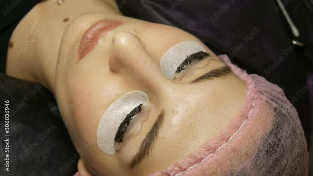 A young woman lies on the procedure for dyeing eyelashes with special black paint A young woman lies on the procedure for dyeing eyelashes with special black paint