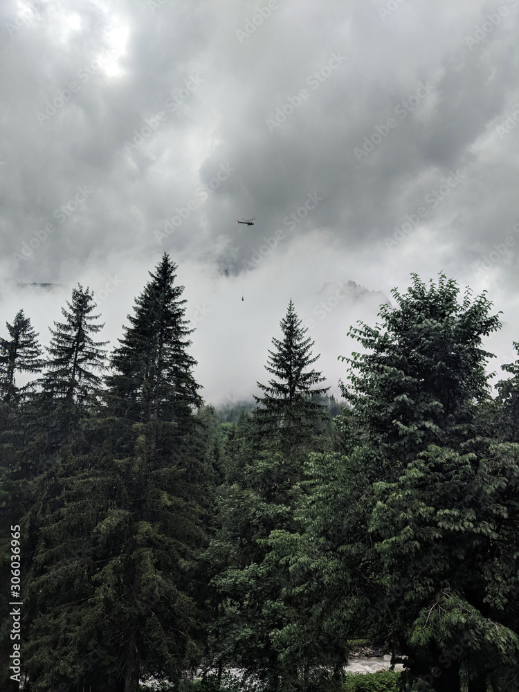 Helicopter carrying goods and flying through the gloomy looking sky over a forest