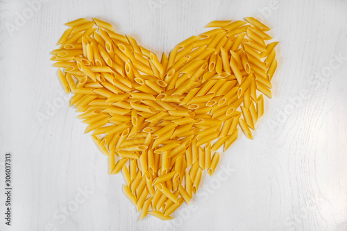 Pasta penne rigate in the shape of a heart on a white background wooden table. Top view, copy space photo