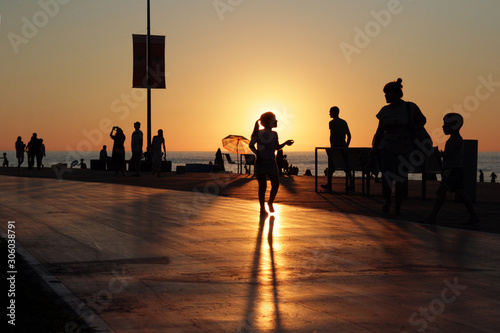 Silhouettes of resting people on sea beach crowdy sunset background