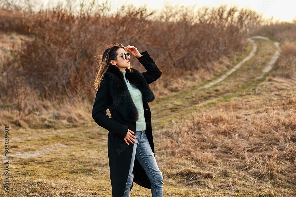 Elegant girl in styilish sunglasses and coat. Beautiful young woman. Autumn landscape.