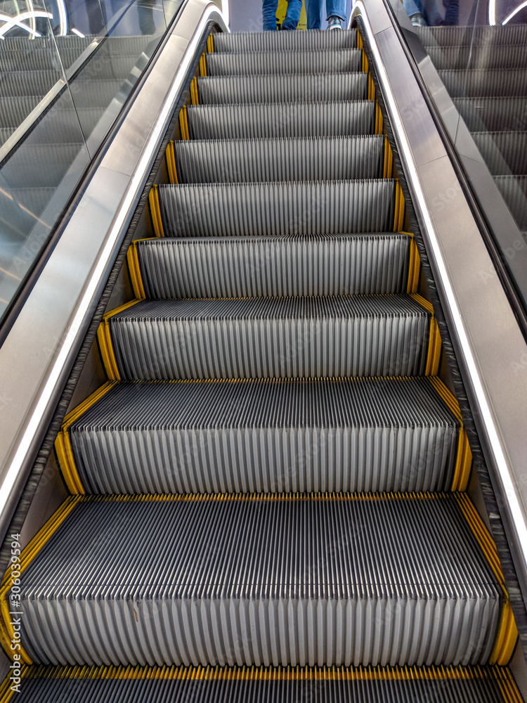 Modern escalator inside a building. Close up of going up electric steps with yellow bands on the side Modern escalator inside a building. Close up of going up electric steps with yellow bands on the side