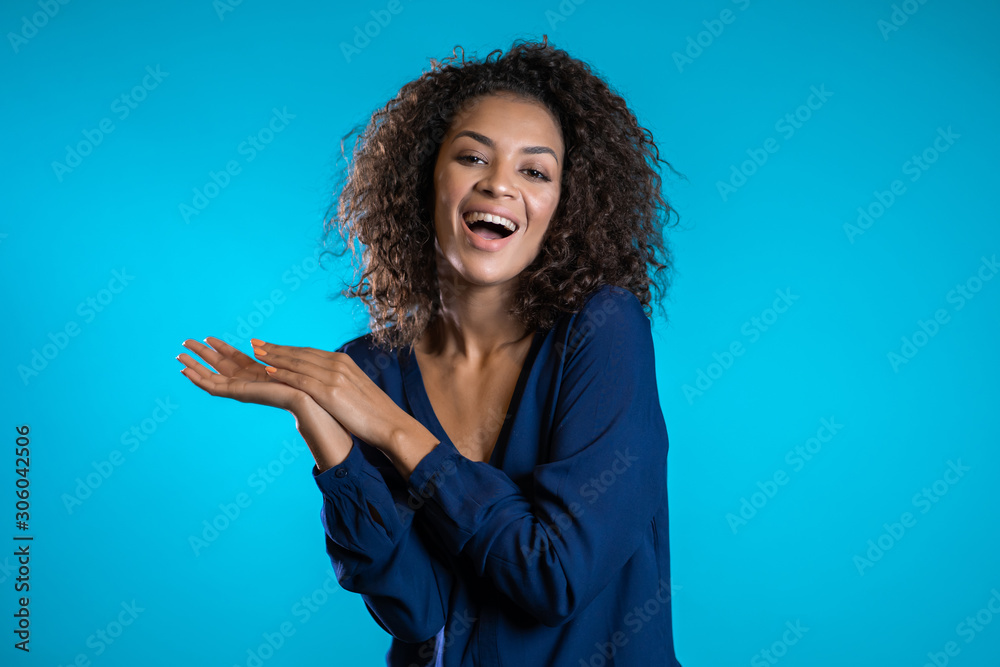 Attractive african american woman with afro hair in business clothing smiling to camera over blue wall background. Cute mixed race girl's portrait Attractive african american woman with afro hair in business clothing smiling to camera over blue wall background. Cute mixed race girl's portrait