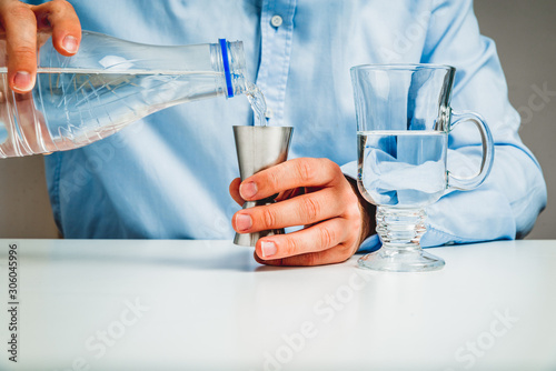 The man pours water from a bottle into a glass. The concept of using and drinking water. Pouring water into a glass. Water problems, saving.