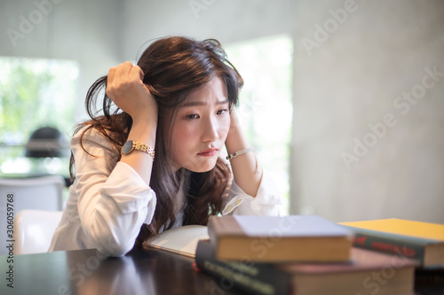 Young Asian girl with stress emotion while reading a lot of books and doing her homework in the university