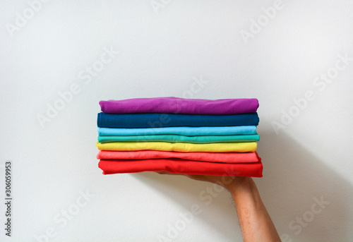 close up stack of folded multicolored t-shirt in hand over white background, copy space