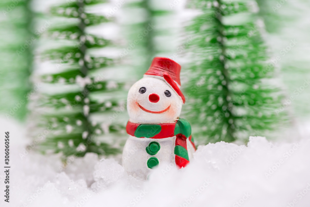 Happy snowman on snow with background of blurred Christmas pine. Miniature people in Christmas Theme.