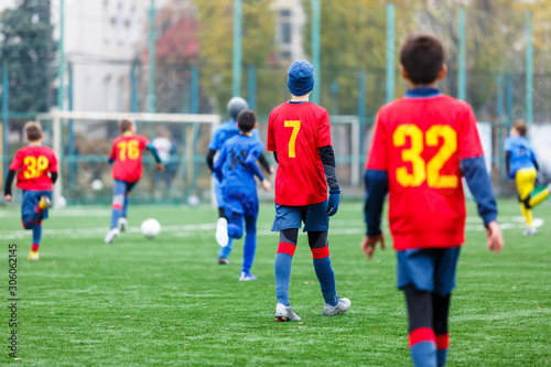 Boys in red and blue sportswear plays football on field, dribbles ball. Young soccer players with ball on green grass. Training, football, active lifestyle for kids concept