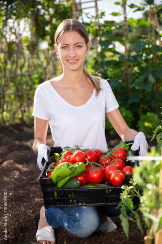Young woman holding basket with harvest of fresh tomatoes and peppers