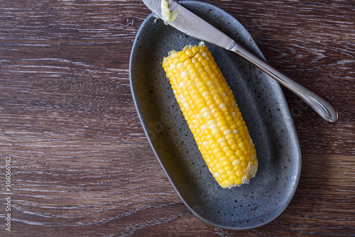 Canvas Print Cooked and buttered corn on the cob on a gray dish, knife with butter