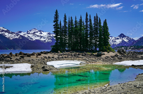 Turquoise coloured lake with trees on the island and snow mountains in Garibaldi provincial park, BC, Canada