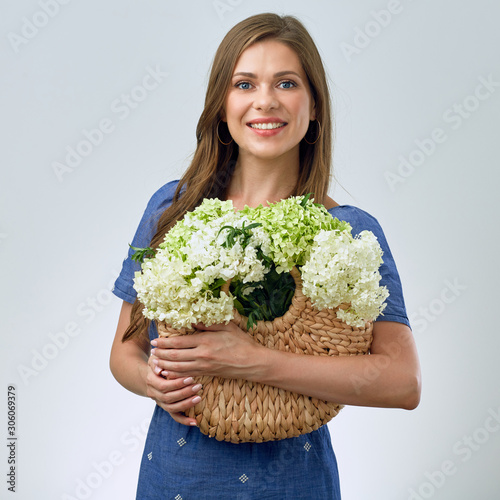 smiling woman holding straw bag with flowers.