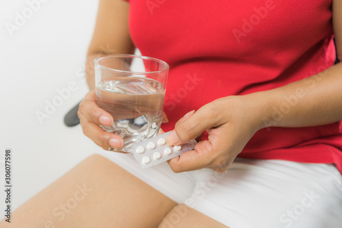 Worried sick young woman holding pill glass of water at home and painkiller for painful periods