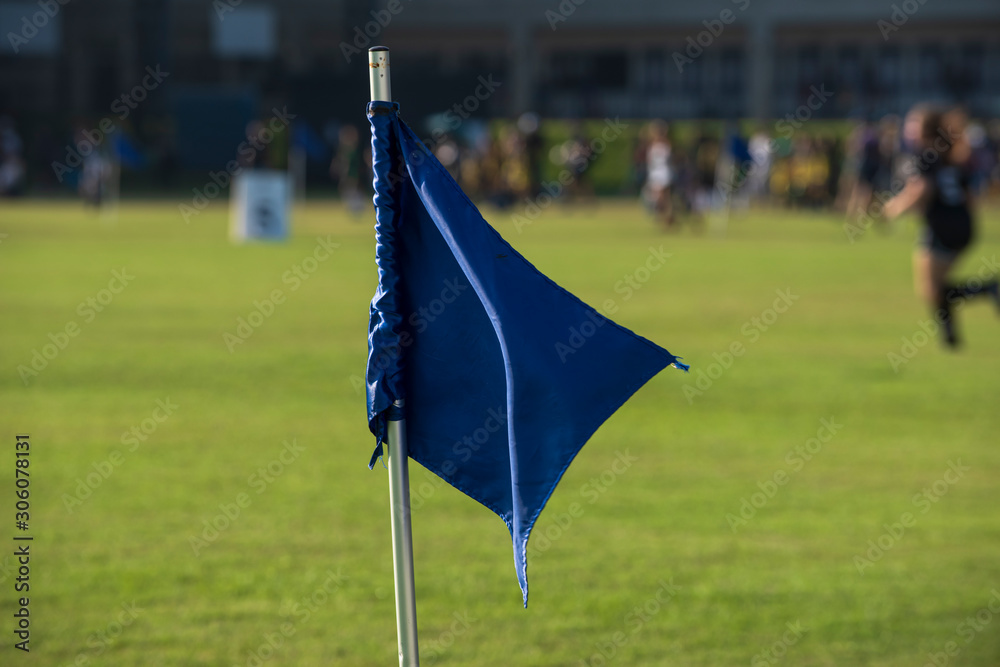 Blue corner flag from a football pitch, seeing group of players, coach, staffs and parents walking and running in a background. Atmosphere from a youth football tournament in summer time.