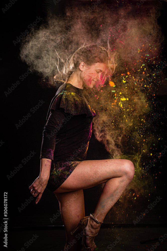 Beautiful young woman Holi paint fest with colorful powder covering her face and a cloud of dust. On black with rainbow bursts of color