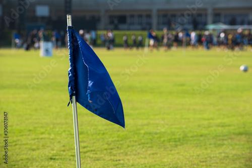 Blue corner flag from a football pitch, seeing group of players, coach, staffs and parents walking and running in a background. Atmosphere from a youth football tournament in summer time.